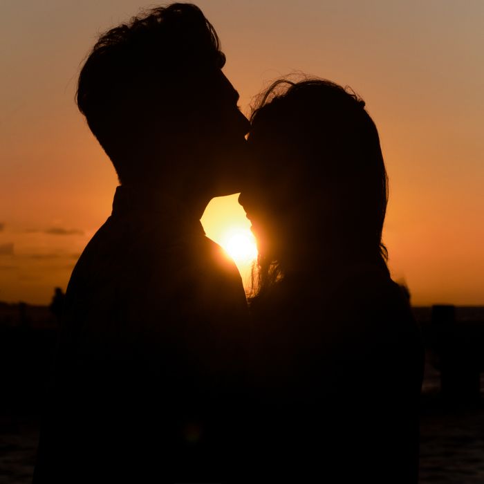 A romantic silhouette of a couple sharing a kiss against a stunning sunset backdrop on the beach.